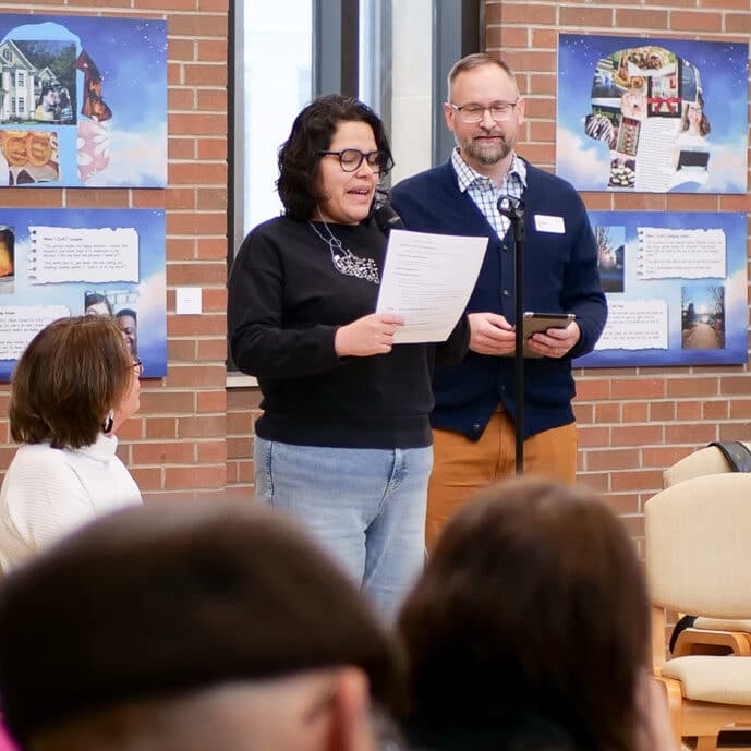 A participant speaks at the Art & Vespers service, with collage panels visible on the wall behind